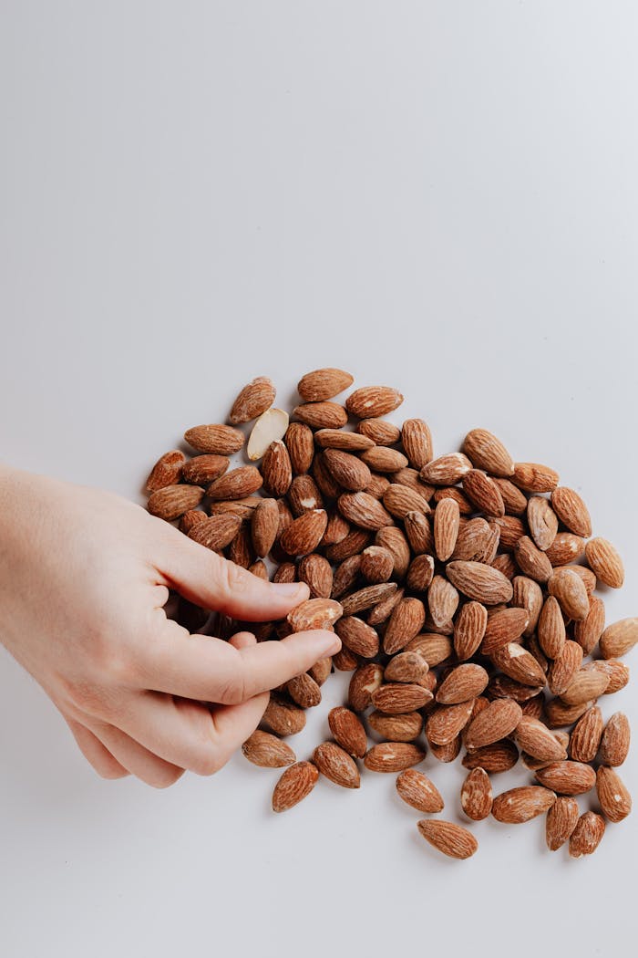 Top view of unrecognizable person taking delicious nutrition almond from pile of nuts placed on white background isolated as healthy food concept